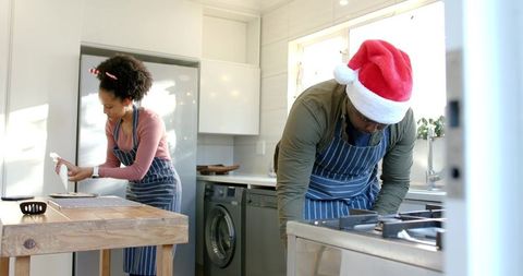 Black couple baking holiday cookies together in bright modern kitchen wearing santa hat
