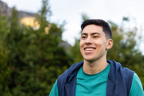 Smiling young man wearing teal shirt and navy vest looking into distance outdoors
