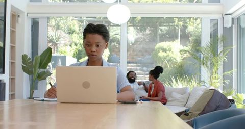 Focused african teen working on laptop while family relaxing in bright modern home