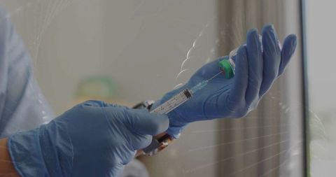 Healthcare worker preparing vaccine syringe wearing blue nitrile gloves with green vial cap