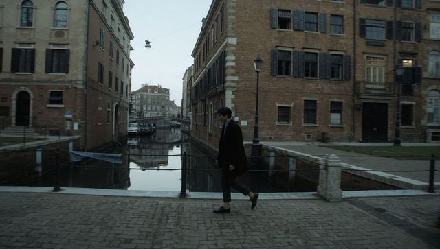 Solitary man walking along canal quay with brick buildings and reflective waterways