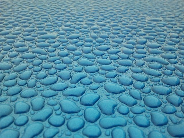 Image of numerous water droplets on a blue surface. This shot highlights the intricate textured pattern created by the droplets. Useful for backgrounds, design elements, and illustrating concepts like moisture, freshness, and cleanliness. Ideal for marketing materials related to water, cleaning products, or technology.
