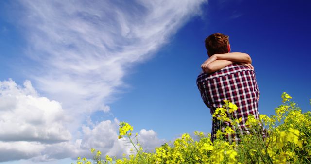 Man hugging partner in a field of blooming yellow flowers with a clear blue sky and white clouds above. Represents love, romance, and nature's beauty. Useful for themes of love, happiness, couples activities, nature outings, and springtime. Perfect for advertisements, blogs, social media posts, and greeting cards themed around relationships and outdoor fun.