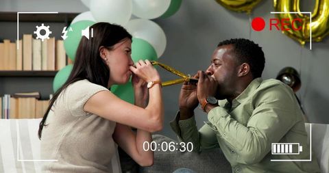 Couple celebrating at home blowing party horns with gold foil balloons and festive decor