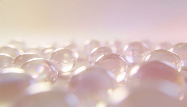 Iridescent glass marbles reflecting pastel light on glossy surface with soft bokeh