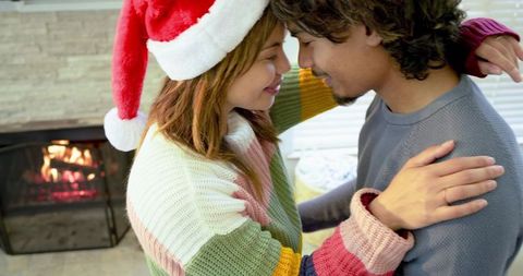 Couple sharing intimate holiday moment wearing santa hat and colorful sweaters by fireplace