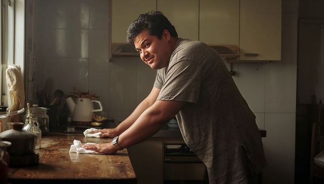 Man wiping wooden kitchen counter, cleaning with cloths in sunlit cozy home lifestyle