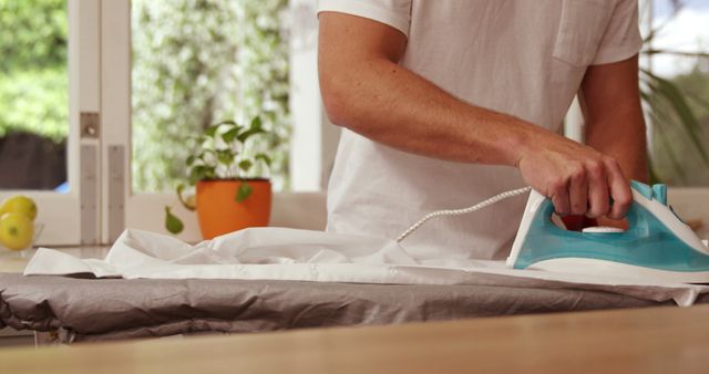 Person Ironing Clothes at Home in Bright Room with Plant - Download Free Stock Images Pikwizard.com