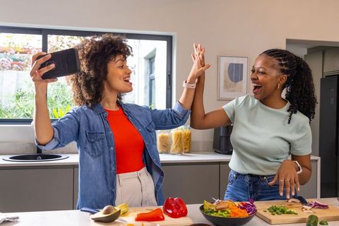African american friends high-fiving while cooking fresh salad on modern kitchen island