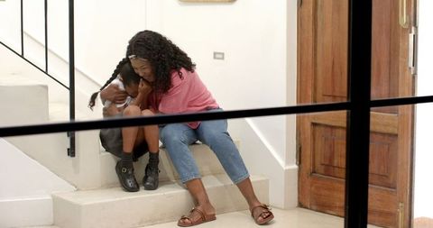 Mother Comforting Daughter on Stairs at Home in Warm Embrace