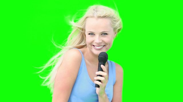 Blonde woman singing and dancing with a microphone in hand against a green screen background. Perfect for music videos, entertainment promos, advertisements, and social media content with customizable backgrounds.