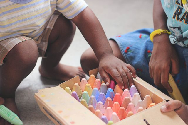 This image captures children's hands reaching for colorful chalks in a close-up shot. It highlights creativity and playfulness, ideal for materials on childhood activities, creativity, outdoor play, or educational resources.