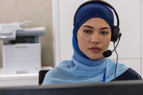 African american customer service agent wearing blue hijab helping customers at office desk