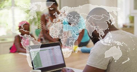 Remote worker analyzing spreadsheet on laptop at home dining table with world map data overlay