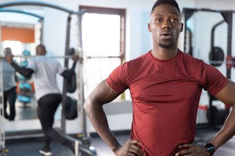 Young african american man resting with hands on hips after weightlifting in gym