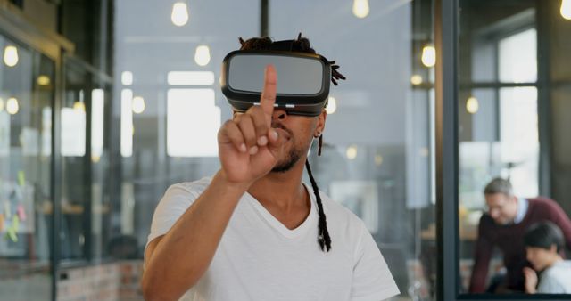 Young man in VR headset interacting with virtual elements in modern office. Ideal for use in content involving technology, innovation, office culture, and the integration of digital tools in professional settings.