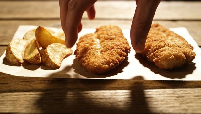 Two fingers reaching crispy breaded cutlets with potato wedges on rustic wooden table