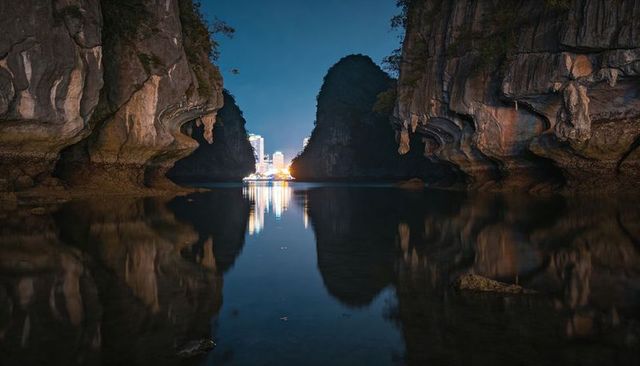 Framing limestone karst cliffs reflecting city lights over calm tidal channel at night