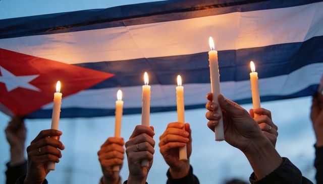 Hands raising lit candles under cuban flag during vigil for unity and remembrance