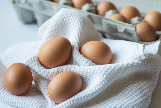 Perfect for use in food-related content, cooking blogs, or organic marketplace ads. Shows fresh, farm-organic brown eggs laid on a white cloth with egg carton in the background, providing a sense of freshness and farm-to-table concept.