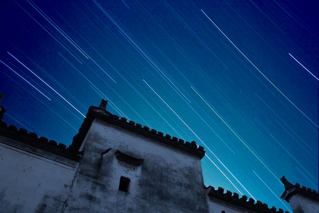 Dynamic long exposure image captures colorful star trails moving across the night sky over traditional architectural rooftops. Perfect for use in travel blogs, astronomy articles, and culture-themed projects to highlight celestial beauty and heritage architecture.