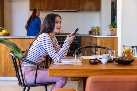 Daughter Using Smartphone as Mother Prepares Drink in Cozy Home Kitchen