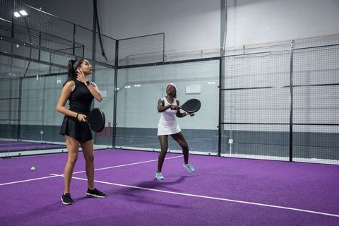 Diverse women playing padel on purple indoor court, teammates returning volley
