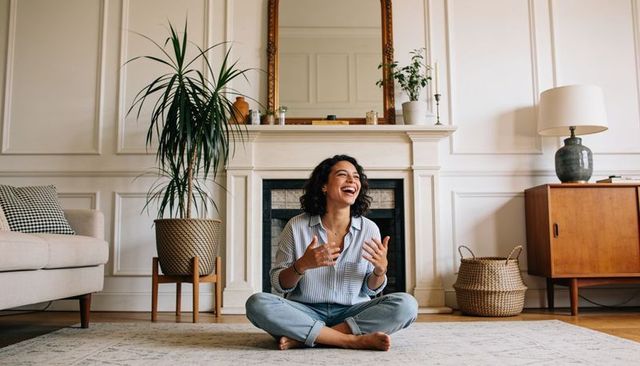 Joyful woman sitting cross-legged in cozy living room with fireplace and midcentury decor