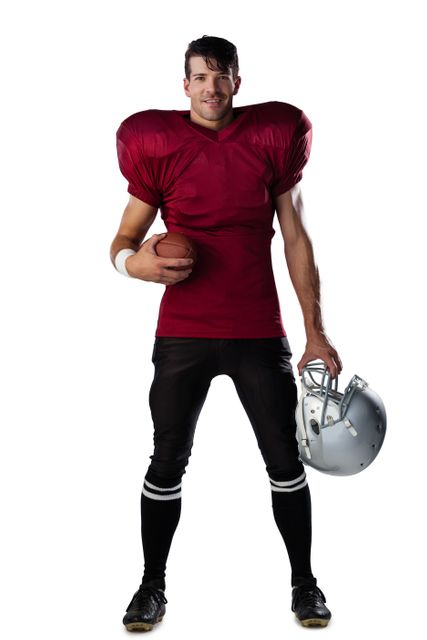 Portrait of smiling American football player holding ball and helmet against white background