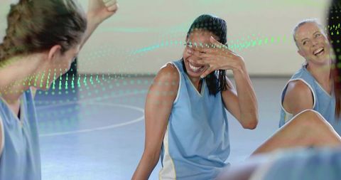 Women basketball team laughing and bonding on indoor court wearing light blue jerseys