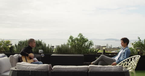 Two Men Relaxing on Rooftop Terrace with Guitar on Cloudy Day