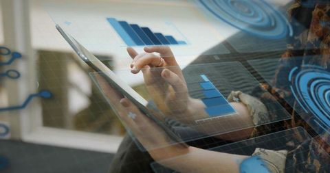 Woman tapping tablet with augmented HUD charts on sofa by window analyzing business data