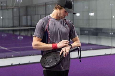 Man checking smartwatch on padel court while holding paddle and wearing red wristband