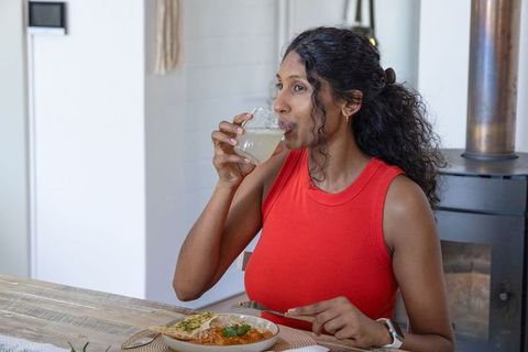 African woman enjoying homemade meal while sipping drink at rustic wooden dining table