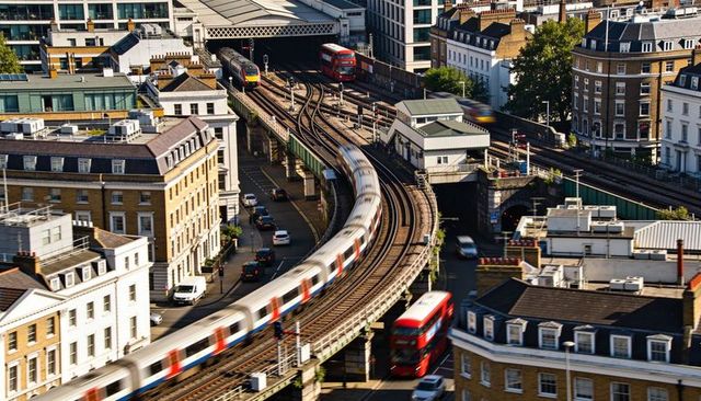 Elevated commuter train curving through london streets with red urban double-decker buses