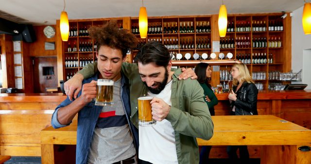 Two friends are enjoying large mugs of beer in a lively and cozy pub with a wooden interior. They are smiling and appear to be celebrating, leaning on each other with arms around their shoulders. In the background, two women engage in conversation, contributing to the casual and cheerful atmosphere. This image can be used to depict friendship, social gatherings, and relaxation in promotional materials for bars, pubs, or social events.