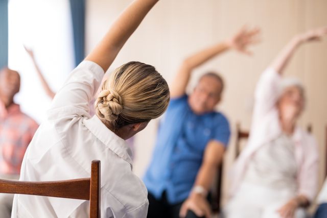Female doctor leading a stretching exercise session with senior individuals in a retirement home. Ideal for use in healthcare, senior care, wellness programs, and physical therapy promotions. Highlights the importance of maintaining an active lifestyle for the elderly.