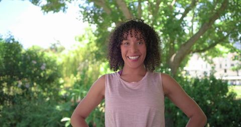 Smiling african american woman standing in park under large tree wearing pink tank top
