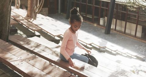 Young student preparing for class on school bench outdoors