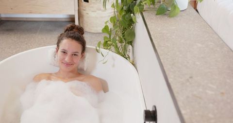 Woman Relaxing in Luxury Bubble Bath with Foam and Indoor Plant