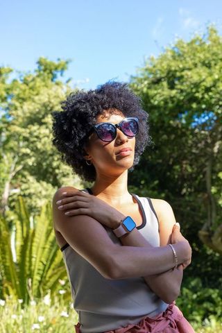 Sunlit african american woman posing in park with mirrored sunglasses and smartwatch