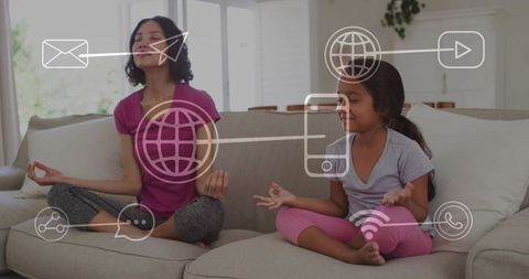 Mother and daughter meditating on sofa with digital icons for mindfulness and tech balance