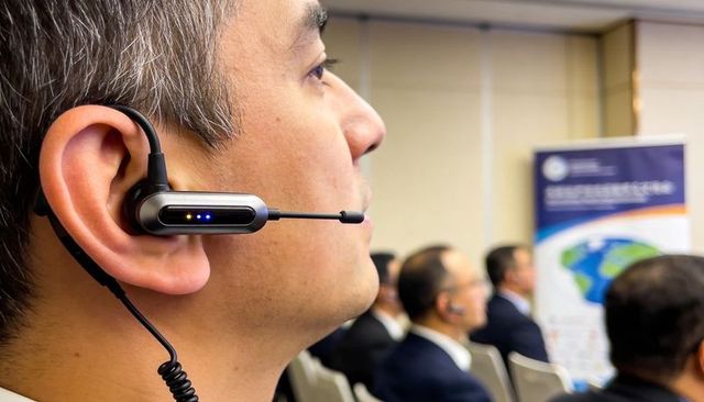 Executive listening with headset microphone during international conference presentation