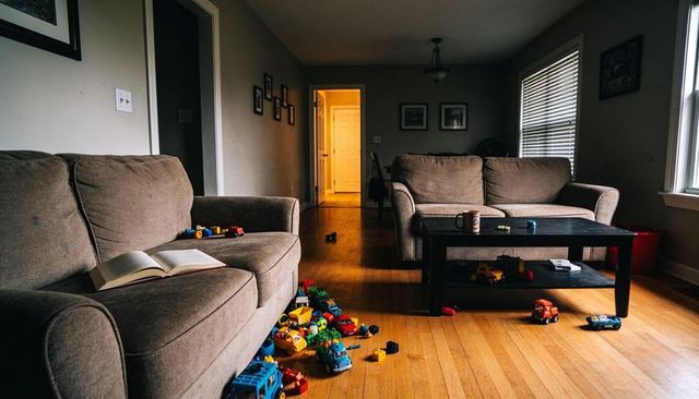 Children's toys scattered across hardwood living room with open book on couch, cozy family playtime