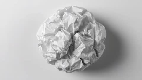 Zooming close-up of crumpled paper ball settling on studio table revealing textured creases