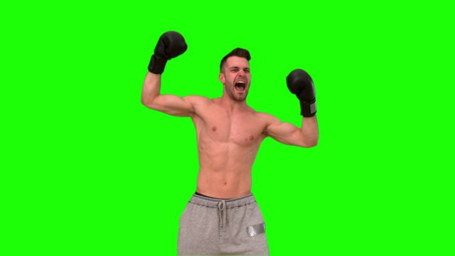 Shirtless man wearing boxing gloves celebrates with arms raised against a vibrant green background. Ideal for creating dynamic sports content or motivational visuals, as the green screen allows for customizable backgrounds and thematic overlays.