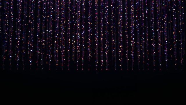 Hanging multicolored led canopy creating floating vertical light curtain in dark gallery