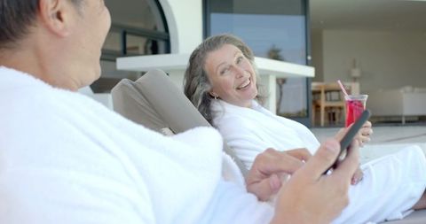 Senior Couple Relaxing in Bathrobes with Smartphone and Drink on Terrace