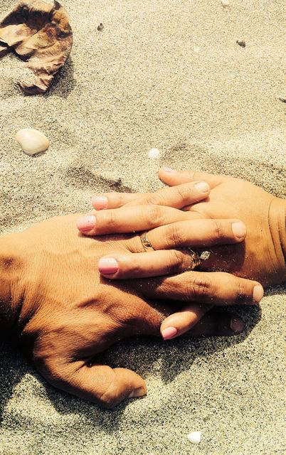 Two hands interlocked, partially buried in sand, symbolizing unity and love. Perfect for themes of romance, relationships, engagement announcements, unity and beach weddings.
