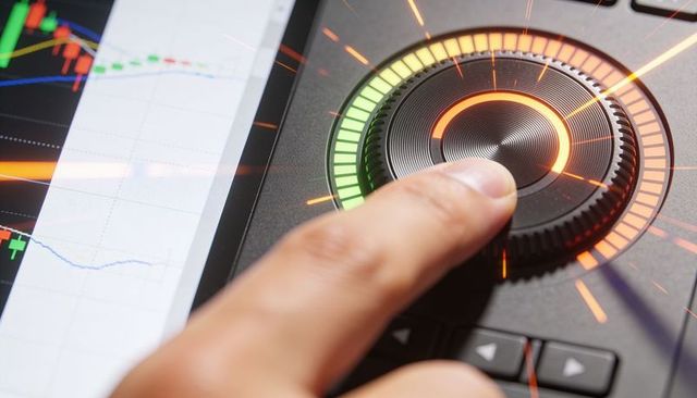 Finger pressing illuminated rotary control dial on trading console with candlestick charts